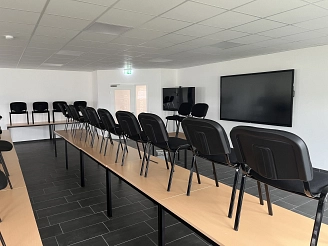 Langer Tisch mit schwarzen Stühlen, dahinter ein großer Bildschirm an der Wand.