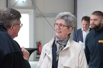 Zwei Personen unterhalten sich, eine Frau lächelt, im Hintergrund stehen weitere Personen.