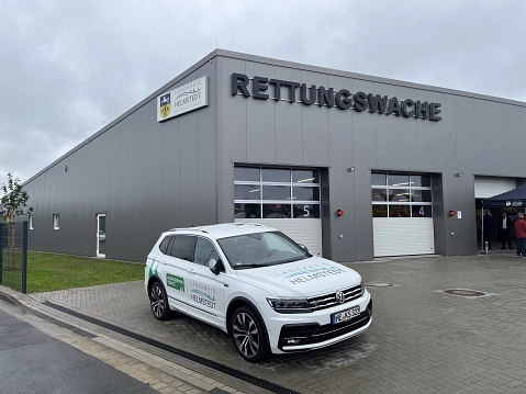 Graues Gebäude mit großem Schriftzug "Rettungswache" und Wappen, geparkt ein Dienstwagen.