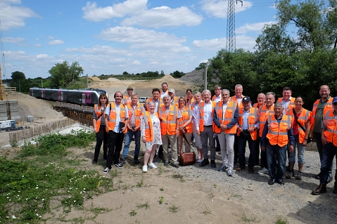 Zahlreiche Politiker der Verbandsversammlung des Regionalverbandes besichtigten die Baustelle an der Weddeler Schleife, während im Hintergrund ein enno auf dem Weg von Wolfsburg nach Braunschweig durchfuhr.