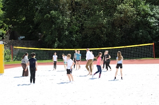 Personen verschiedener Altersgruppen spielen Volleyball auf einem Sandplatz.